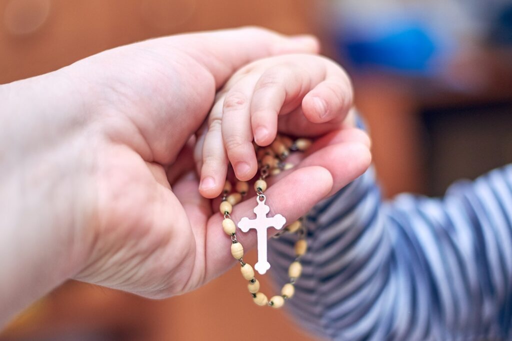 A small child takes a rosary from his dad's hand